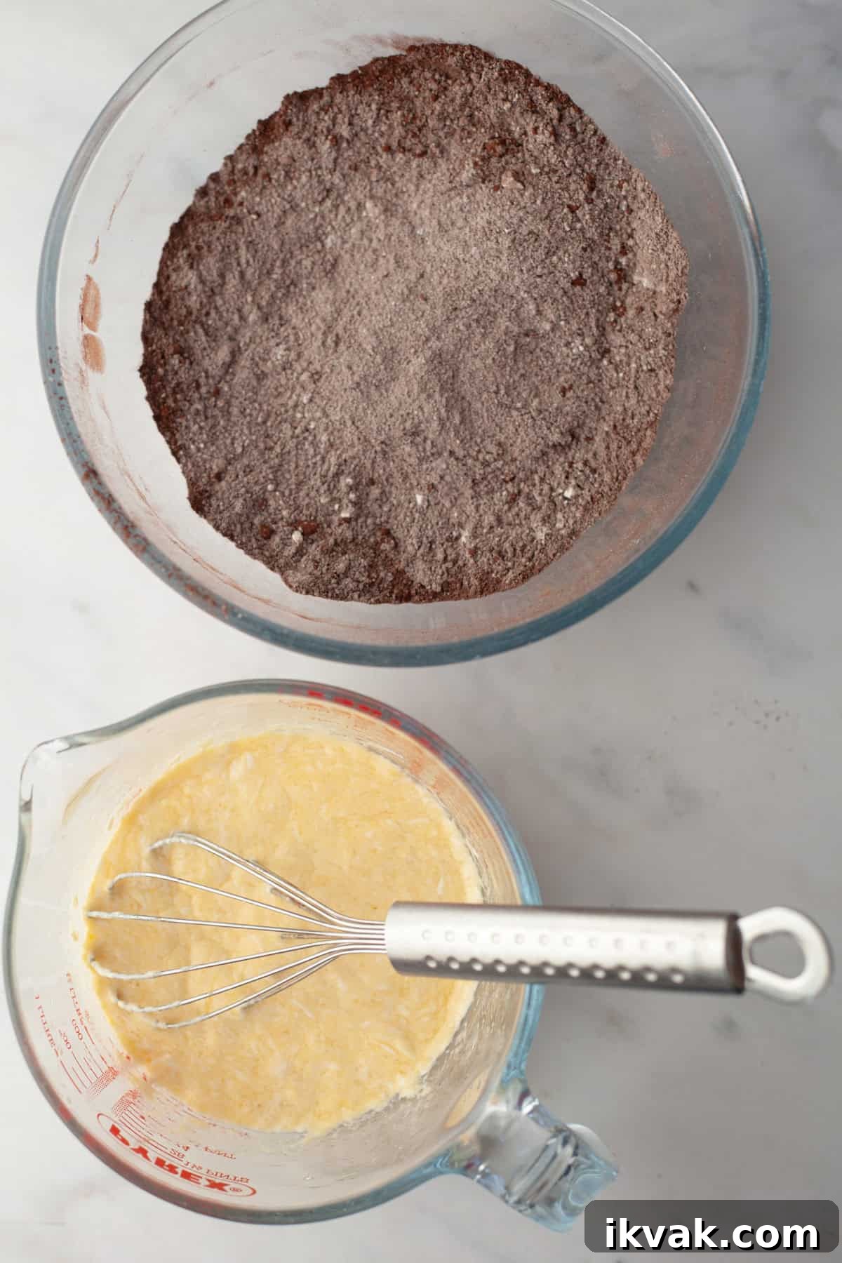 A glass bowl with cocoa powder and flour and a glass jug with a pale yellow mixture in it.