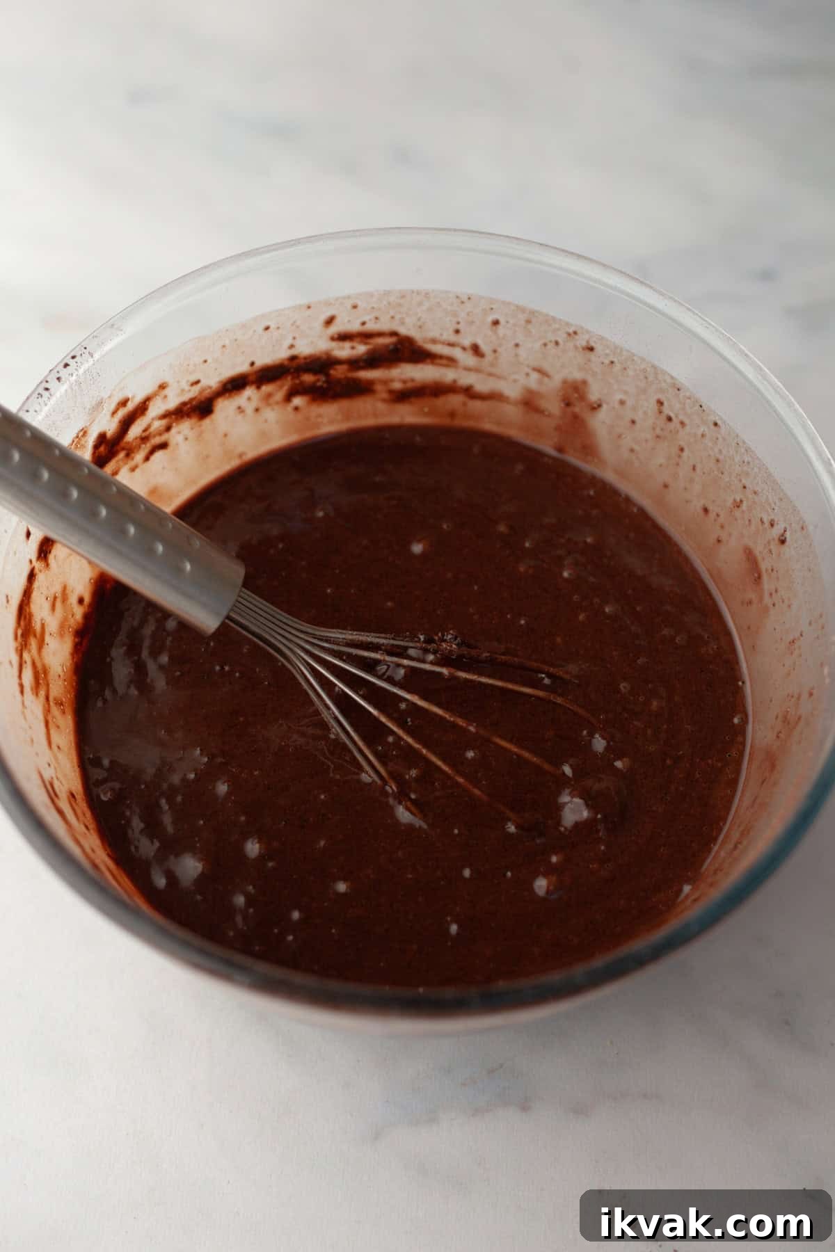 Chocolate cupcake batter in a glass bowl with a whisk.