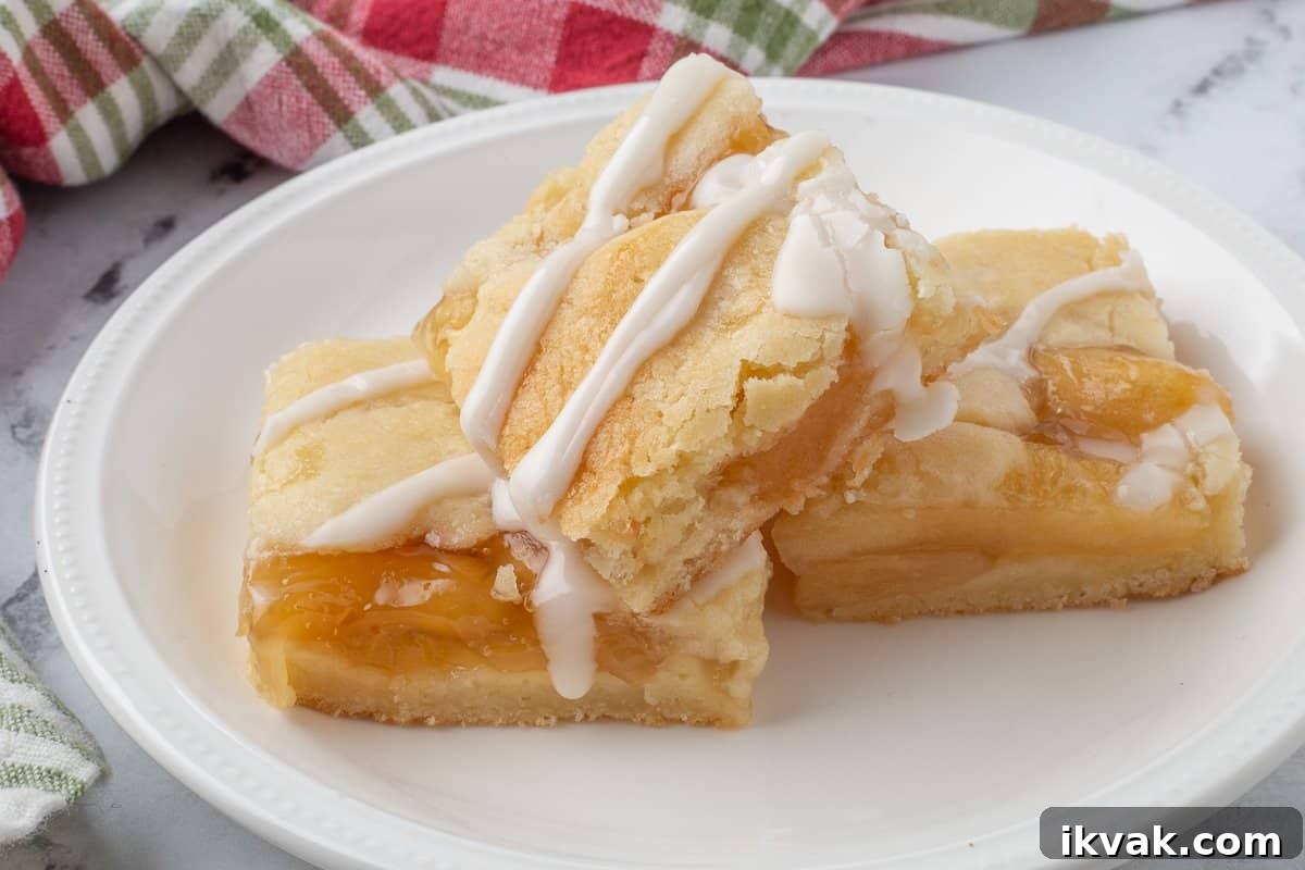 Three apple pie bars on white plate with vanilla glaze.