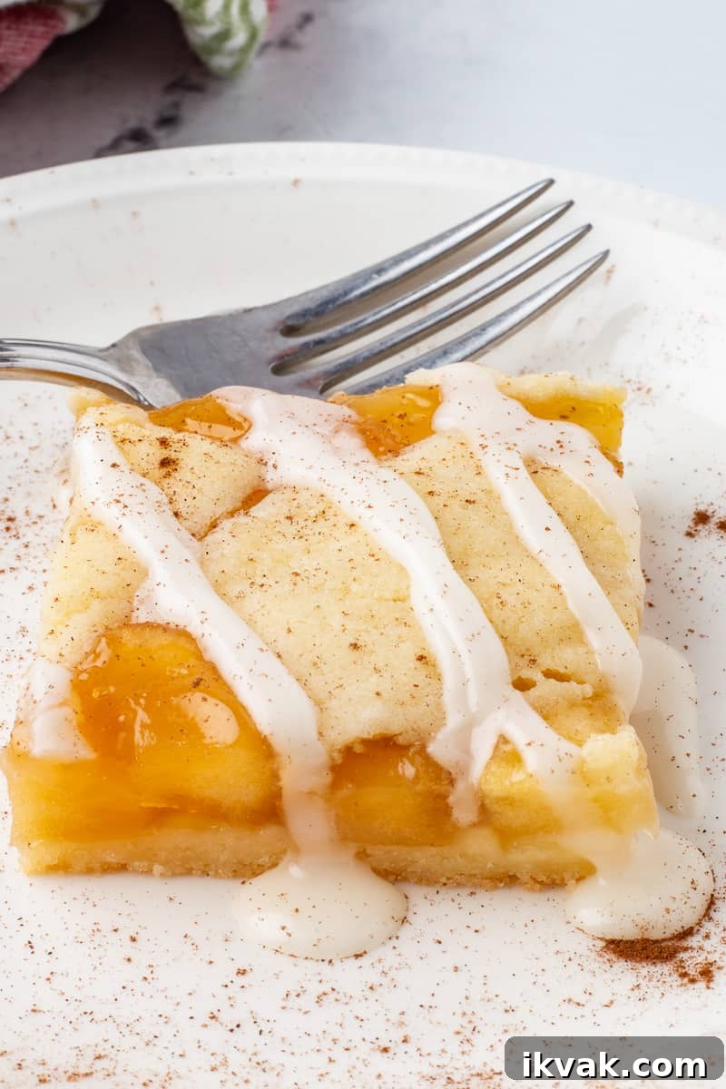 Close up image of apple pie bars on white plate with fork.