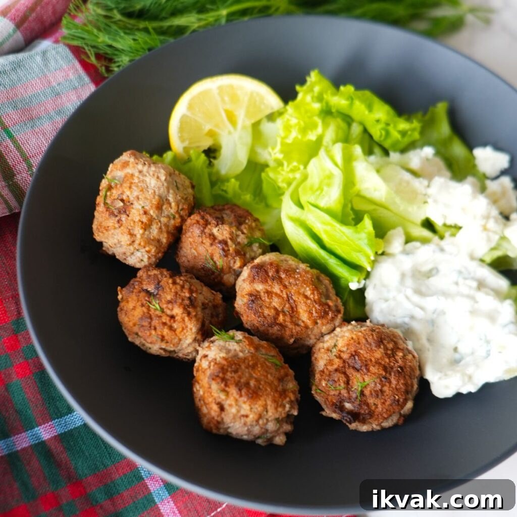 Greek turkey meatballs with tzatziki sauce, fresh dill garnish, and a side salad on a black plate.