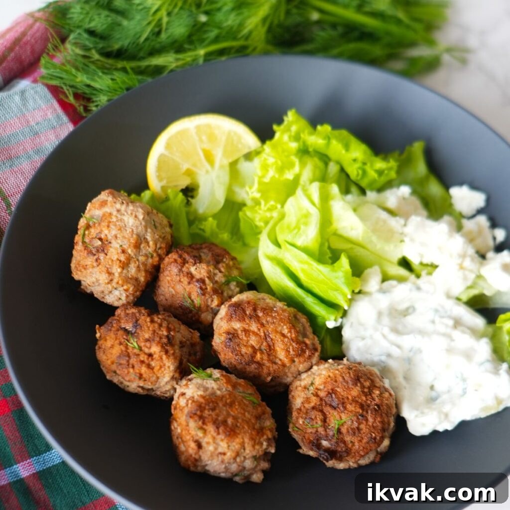 Greek turkey meatballs with tzatziki sauce, fresh dill garnish, and a side salad on a black plate.