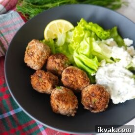 Greek turkey meatballs with tzatziki sauce, fresh dill garnish, and a side salad on a black plate.
