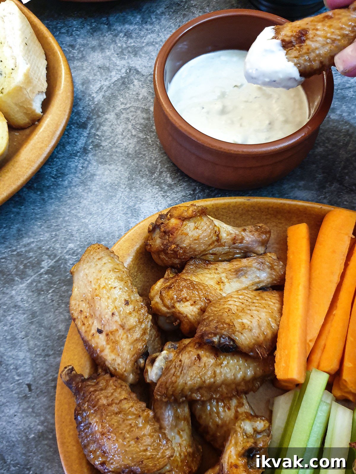 A chicken wing being dipped in blue cheese sauce, next to a plate of wings.