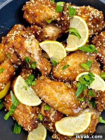 A black serving dish piled with honey lemon chicken wings garnished with lemon slices and chopped parsley.