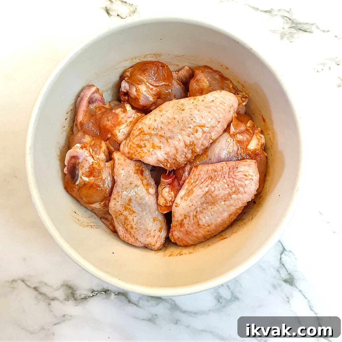 A mixing bowl containing chicken wings which have been rubbed with salt and paprika.
