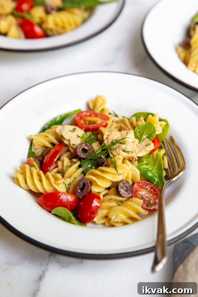 Close up of a bowl of pasta salad in a serving bowl with a fork. 