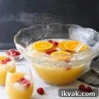 A punch bowl of mimosa punch with extra oranges and raspberries and two glasses full of punch
