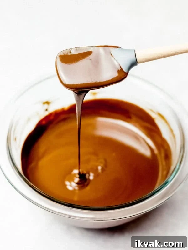 chocolate ganache dripping off a spatula into a glass bowl