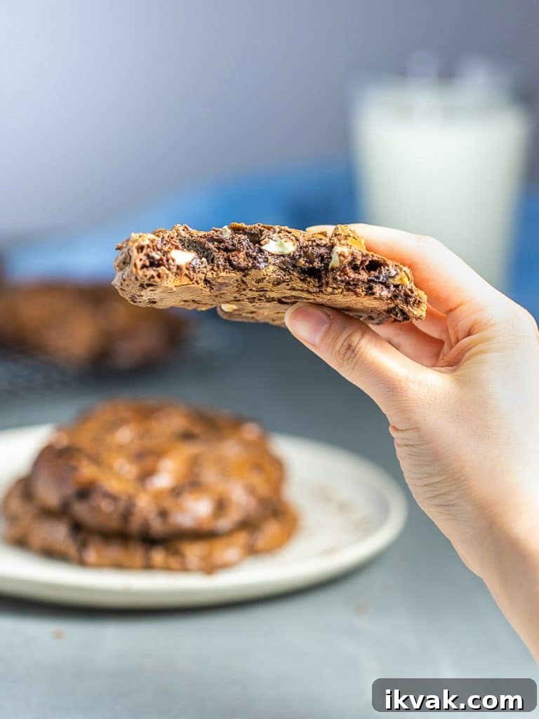 chocolate cookie held in hand with plate of chocolate cookies and milk in the back