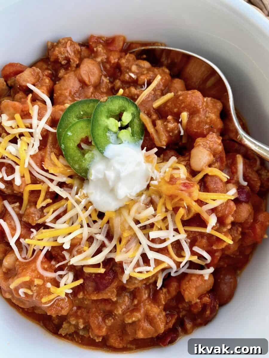 A bowl of chili with toppings and a spoon on the side