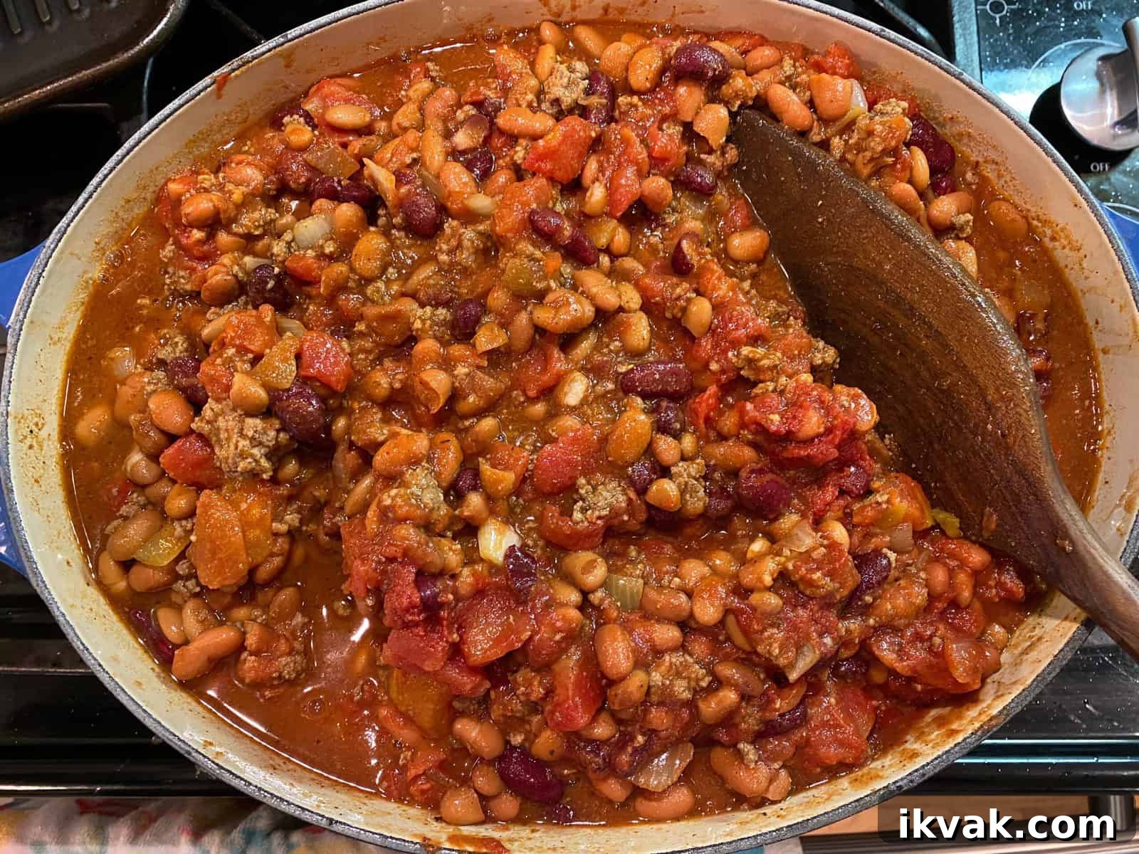 A large pot of chili on the stove with a wooden serving spoon.