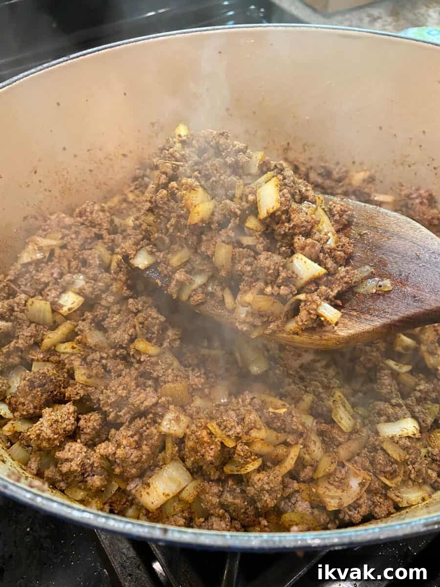 Chili meat and onions browned and steaming in a pot on the stove.