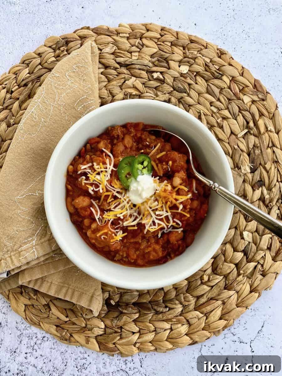 A bowl of chili on a placemat with a napkin on the side of the bowl and a spoon in the chili