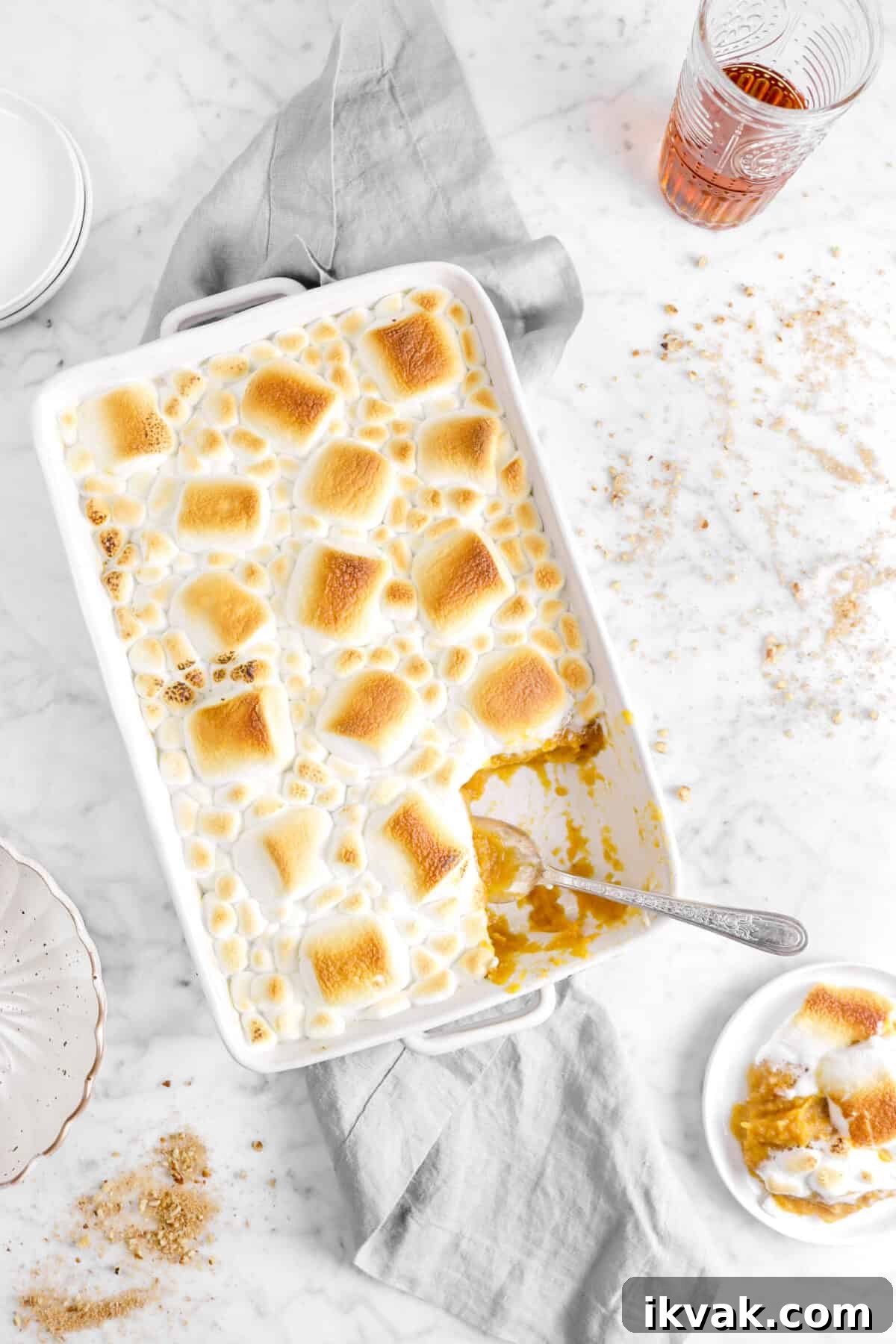 overhead shot of sweet potato casserole with roasted marshmallows on a grey napkin with some on a plate and glass of bourbon