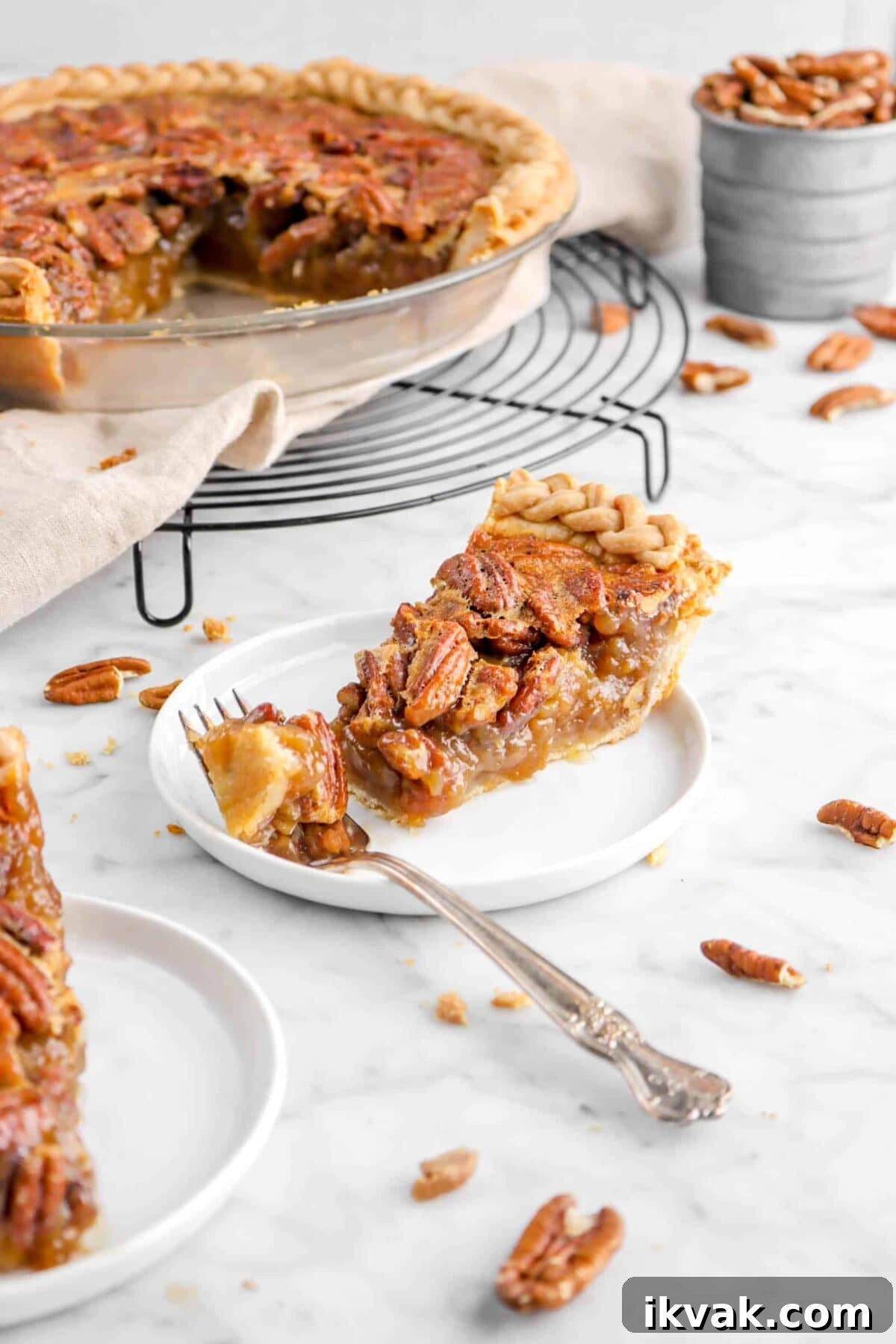 slice of pecan pie with fork on white plate with pecan pie behind