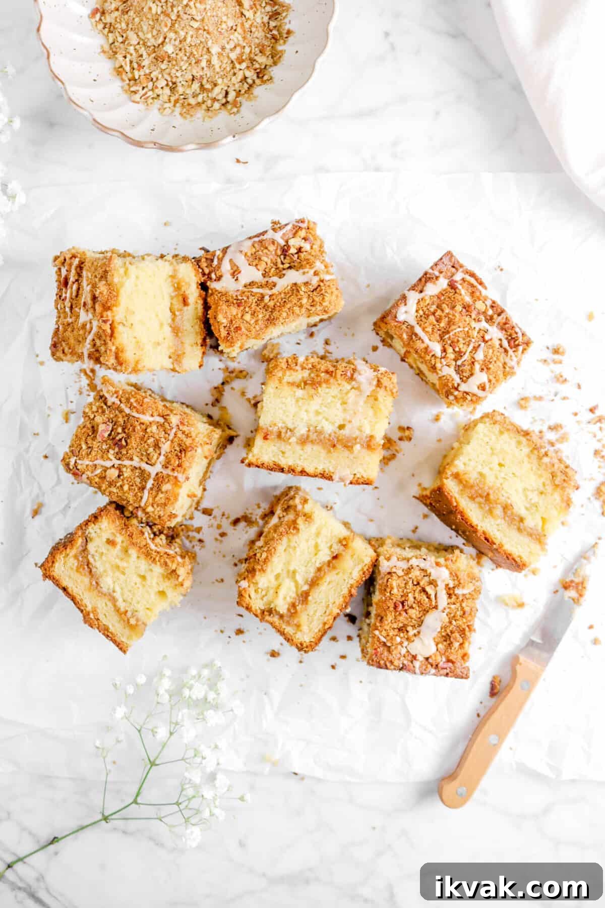 nine slices of apple pie coffee cake on parchment with streusel, a knife, and flowers