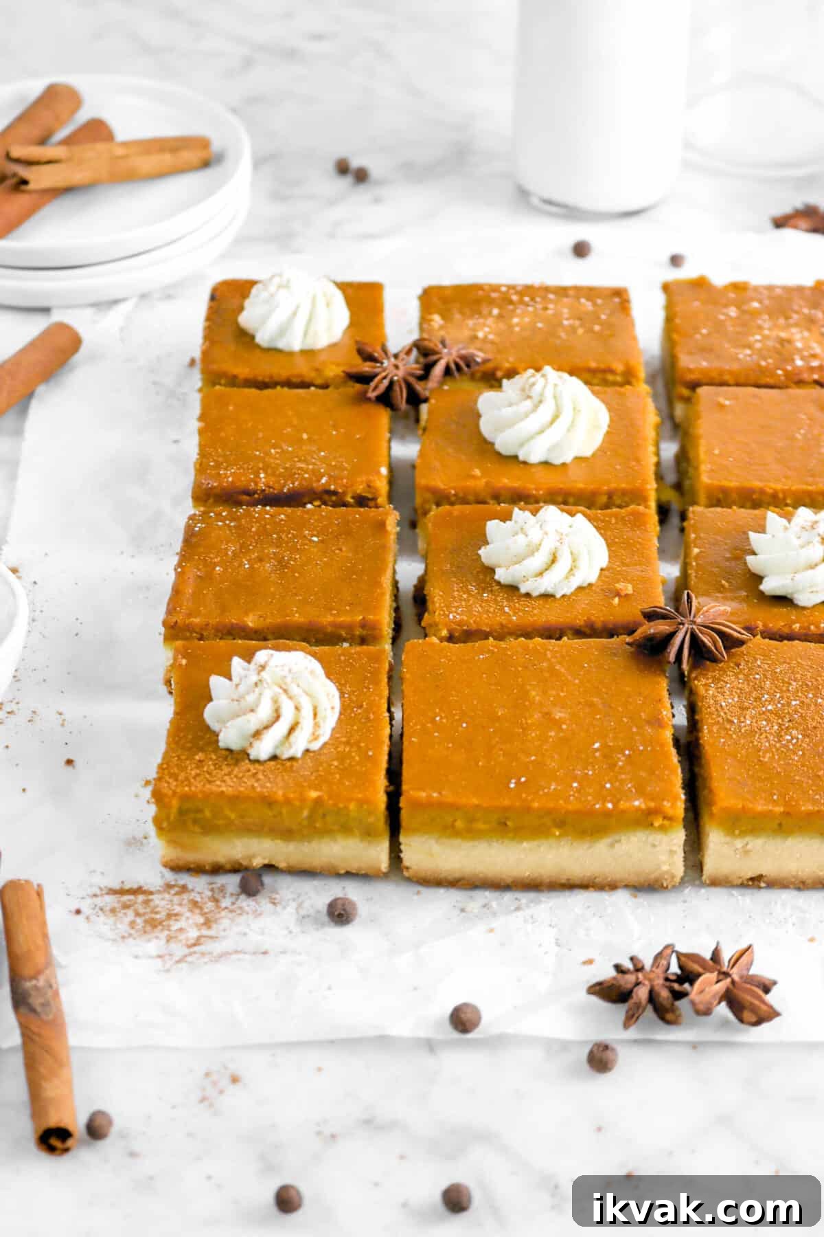 twelve pumpkin pie bars on parchment paper with whole spices, plates, and milk glass