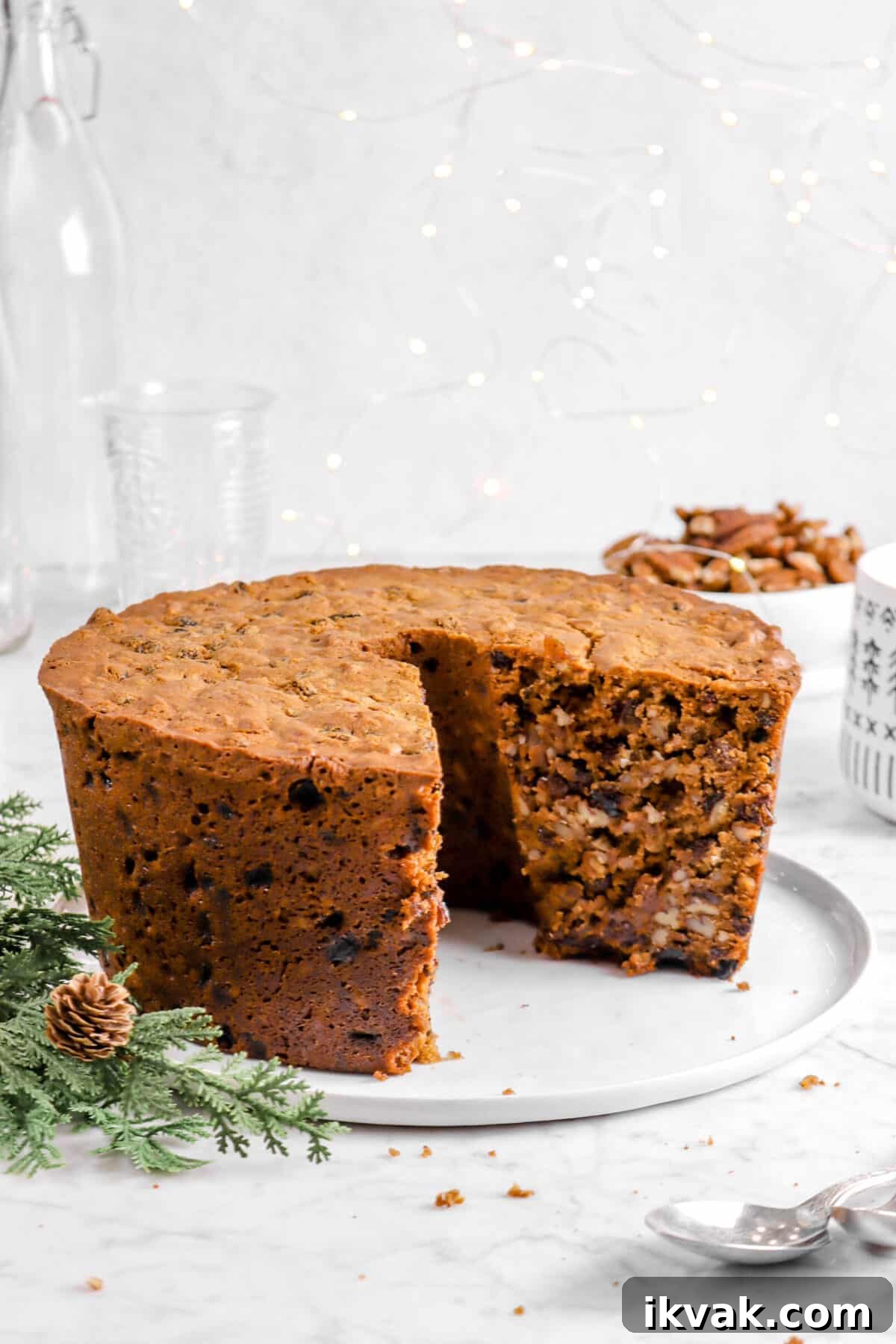 nut cake with a slice taken out of it on a white plate with fairy lights, greenery, and glasses