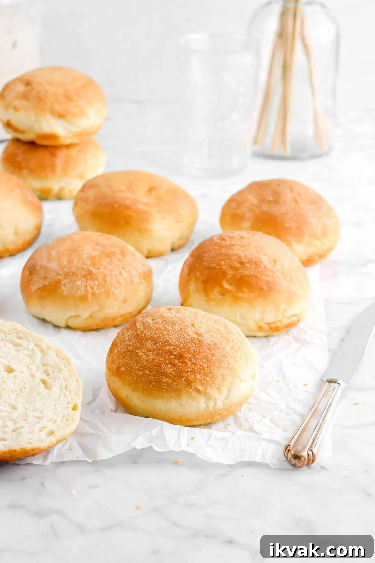six hamburger buns on parchment paper with two stacked behind and a knife