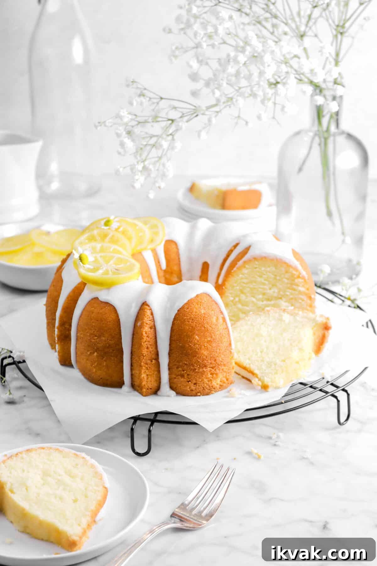 bundt cake on wire cooling rack with flowers, a slice in front, slice behind, and candied lemon slices