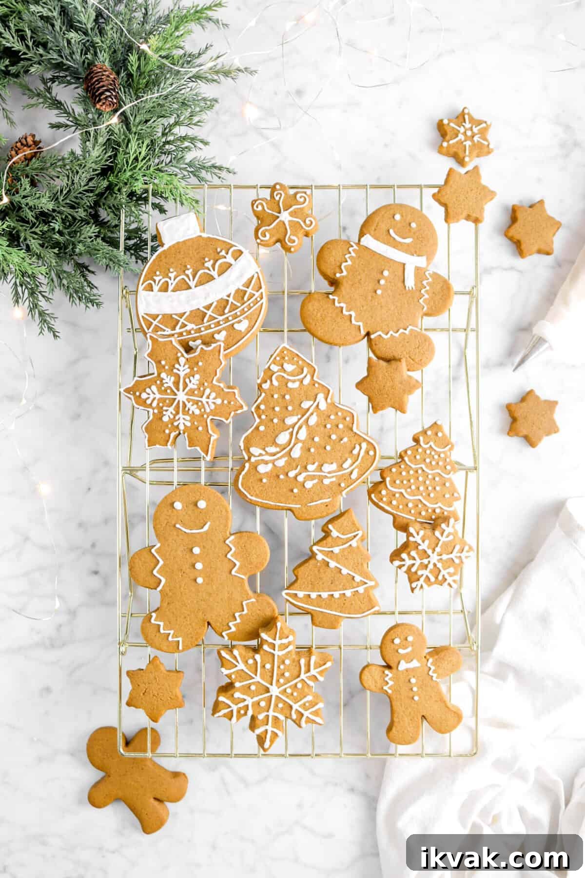 iced gingerbread cookies on gold cooling rack with napkin, greenery, lights, and piping bag