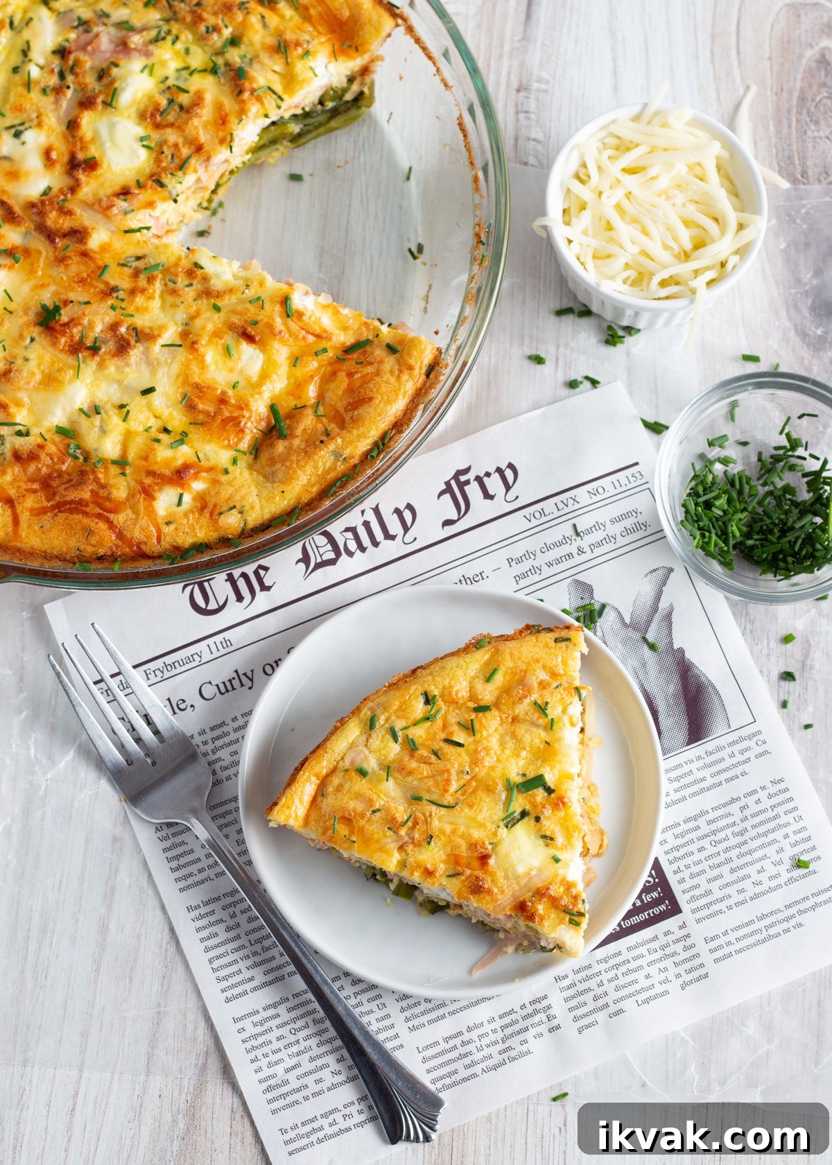Asparagus, Ham & Goat Cheese Crustless Quiche Recipe 11 Picture with a slice of crustless quiche with asparagus ham and goat cheese with rest of quiche in background and little bowls with cheese and chives.