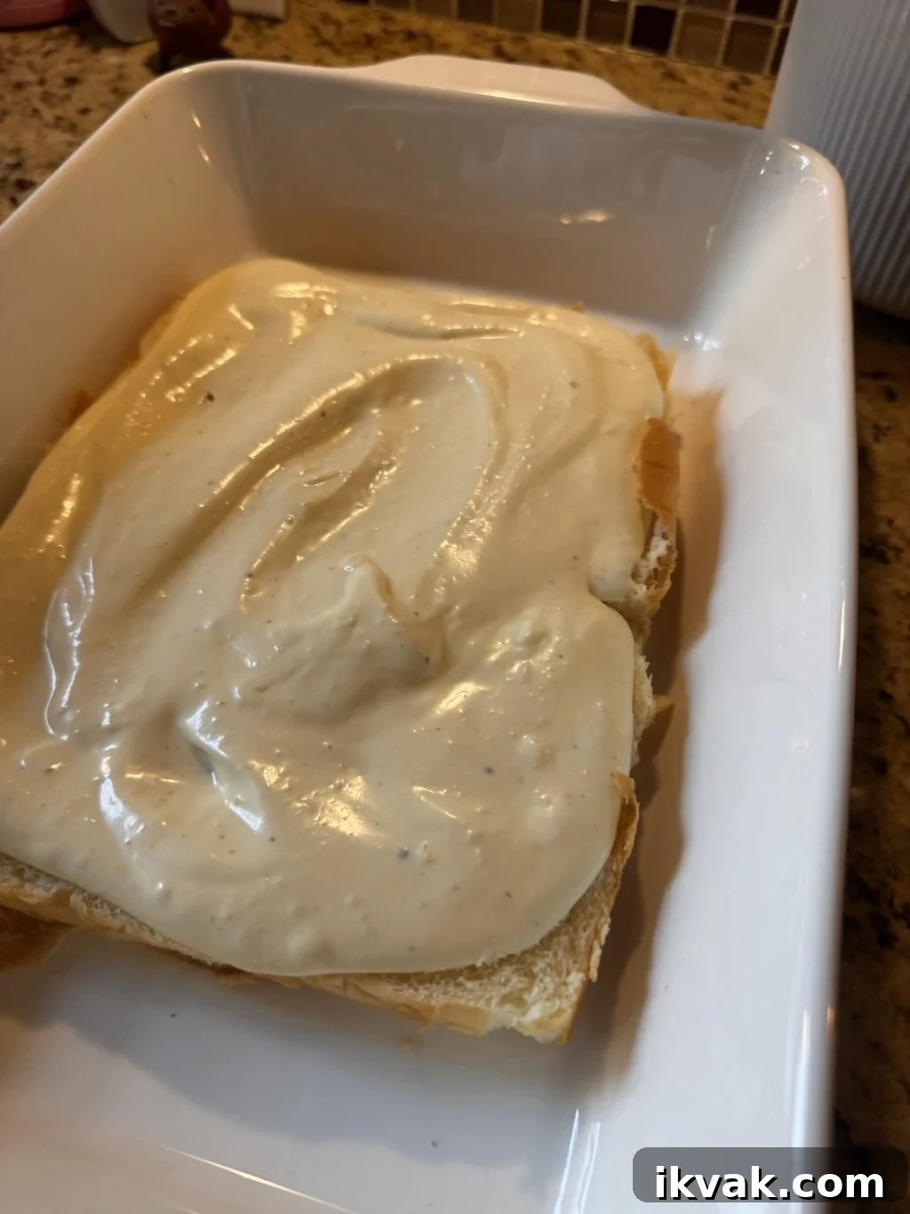 The half slab of Hawaiian Rolls with the cream cheese mixture spread out over it in a baking dish.