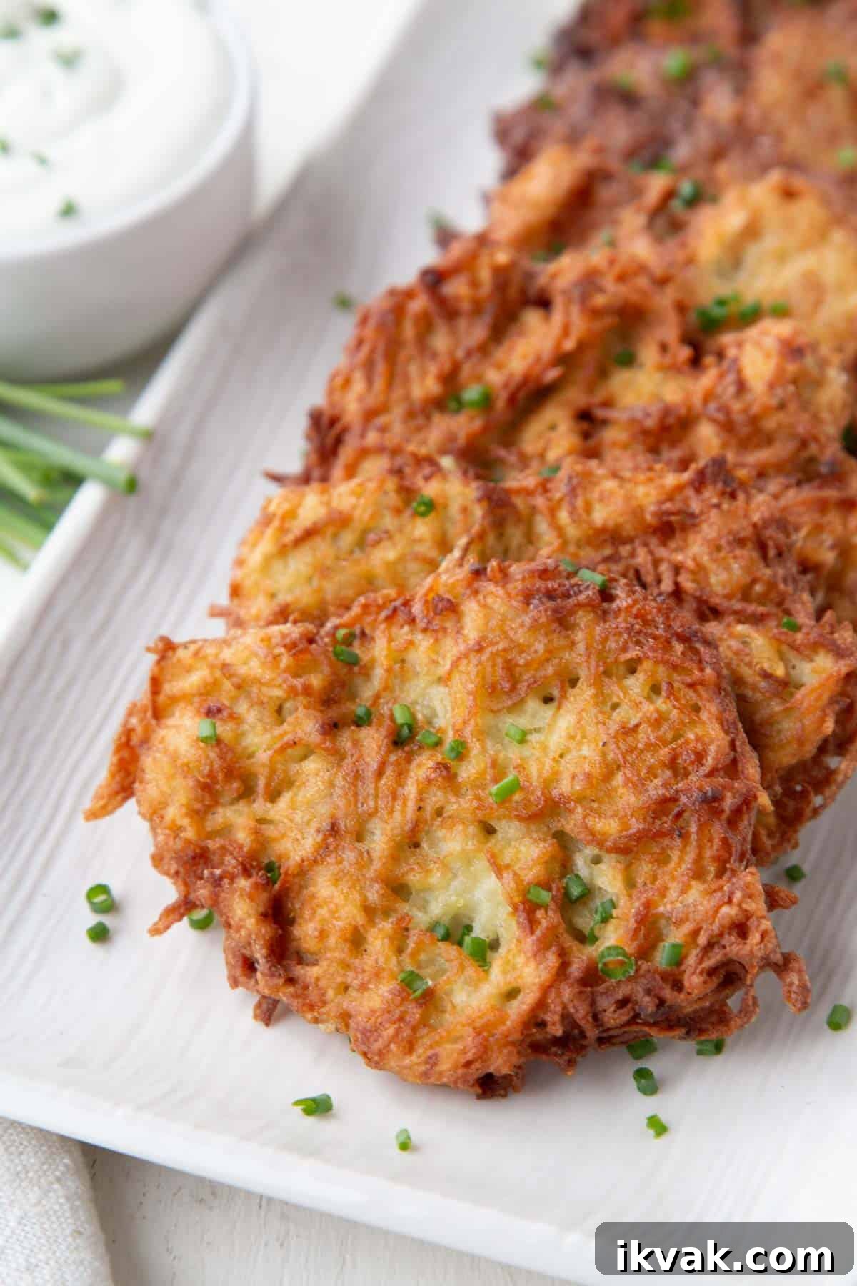 Crispy Potato Pancakes Recipe: Golden Hash Browns from Scratch 2 crispy potato pancakes with a golden brown exterior on a white platter, topped with chopped chives.