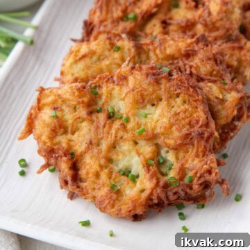 Crispy Potato Pancakes Recipe: Golden Hash Browns from Scratch 13 crispy potato pancakes topped with chopped chives on a white platter.