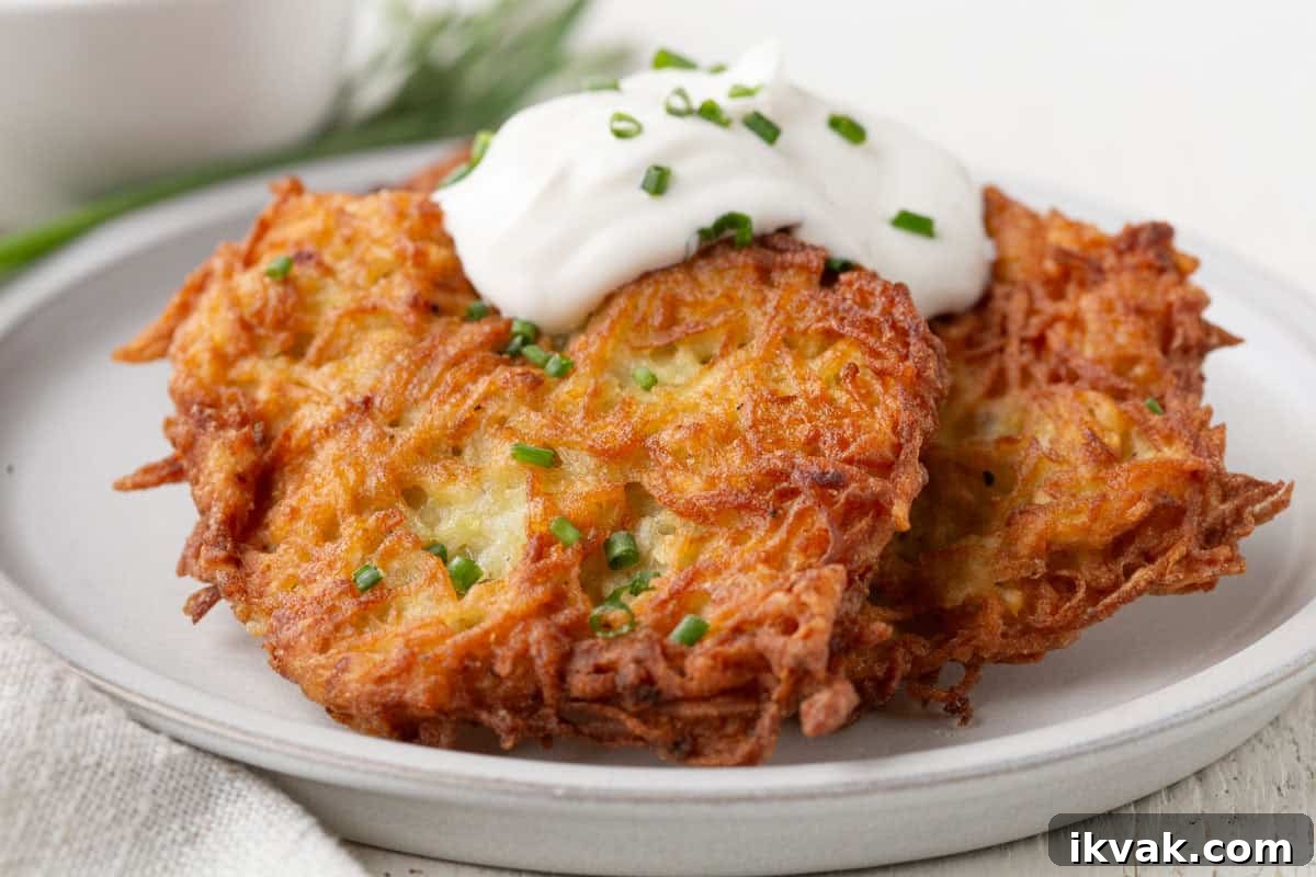 Crispy Potato Pancakes Recipe: Golden Hash Browns from Scratch 4 potato pancakes with golden brown edges, topped with a dollop of sour cream and chopped chives.