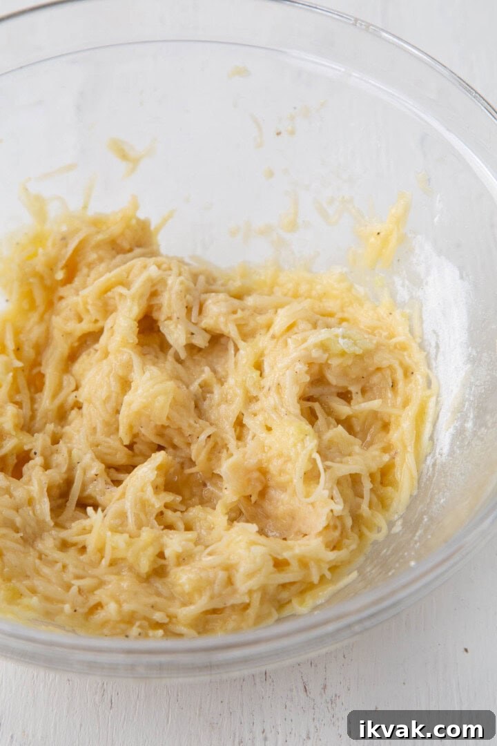 Crispy Potato Pancakes Recipe: Golden Hash Browns from Scratch 8 shredded potatoes in a pancake batter in a glass bowl.