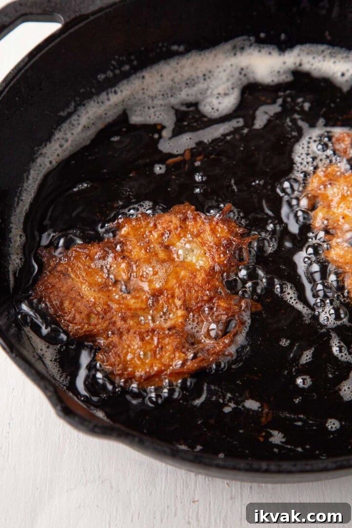 Crispy Potato Pancakes Recipe: Golden Hash Browns from Scratch 10 potato pancakes frying in oil in a cast iron skillet, crispy and golden brown.