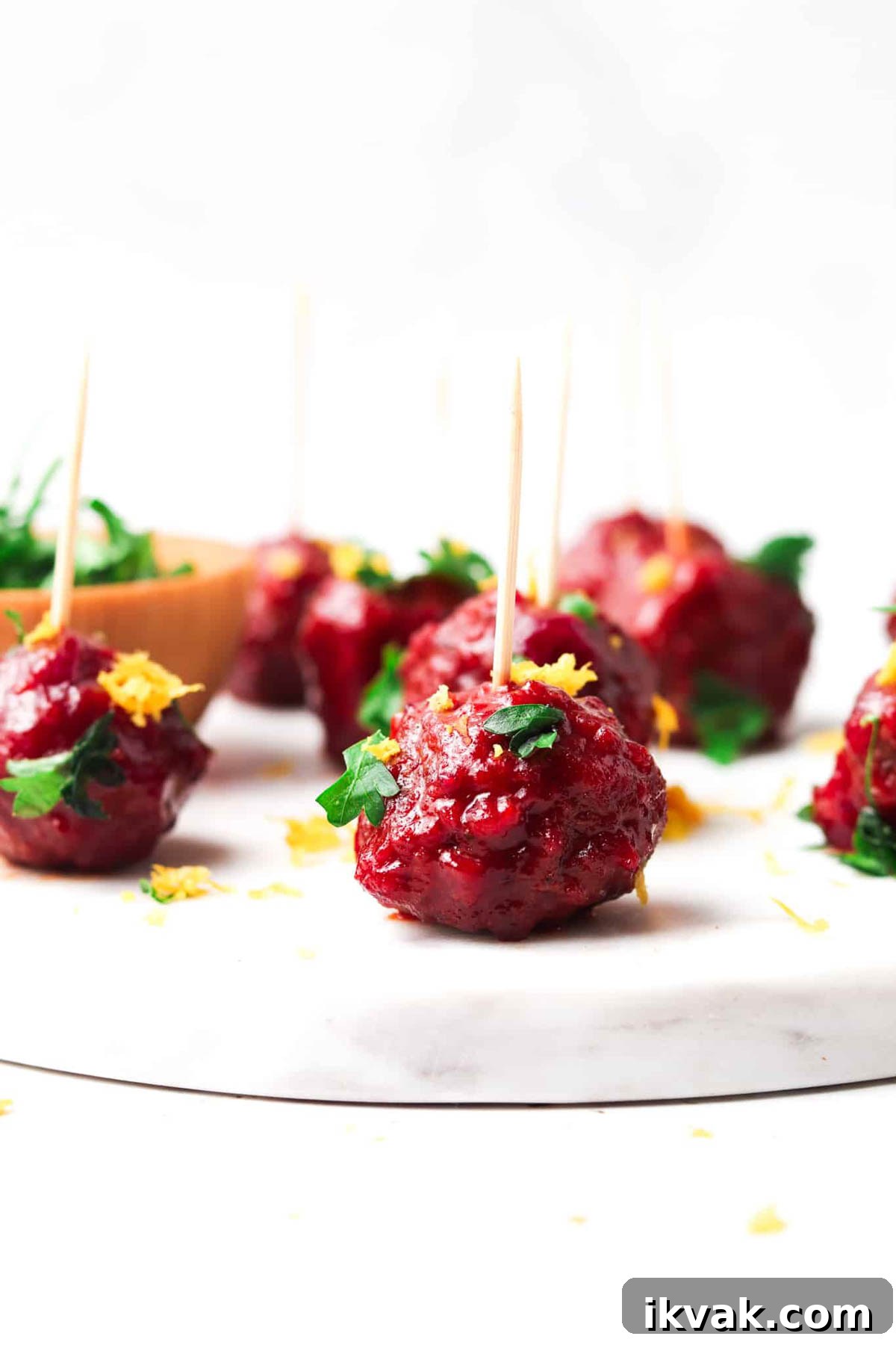 Sweet Cranberry BBQ Meatballs for Parties and Weeknights 2 Cranberry BBQ meatballs garnishes with fresh green herbs and citrus zest with a toothpick in them.