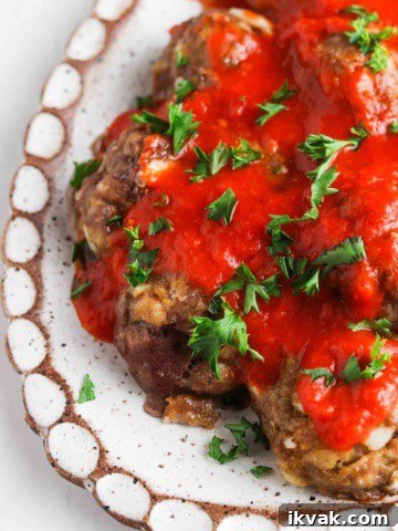 Gluten free meatballs on a white plate covered in red sauce and parsley.