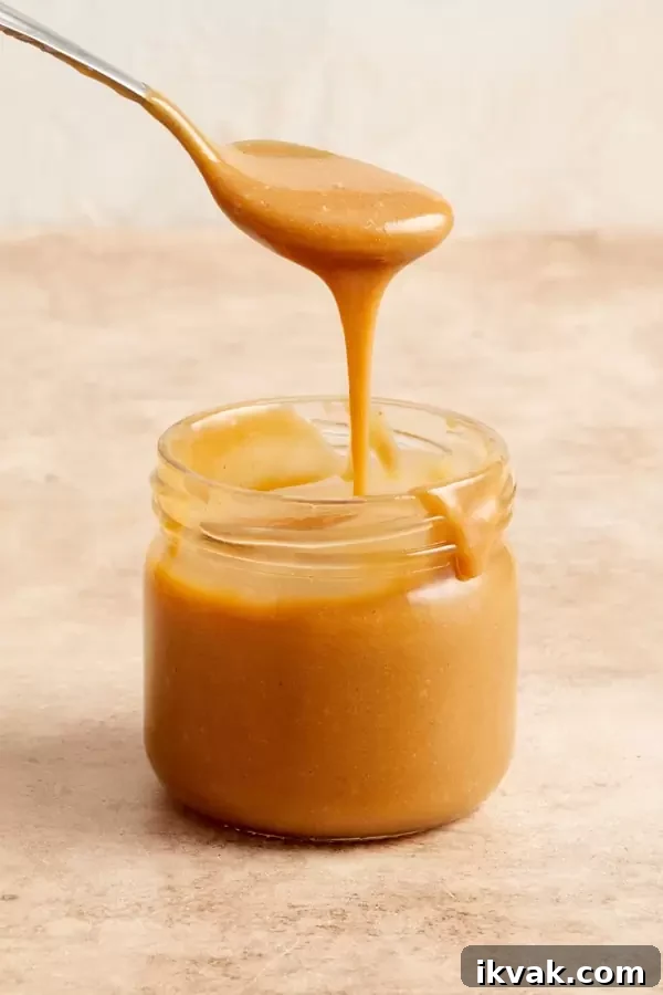 A jar of Dairy Free Caramel Sauce with some being drizzled with a spoon.