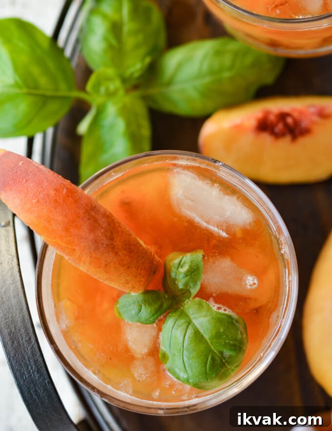 A top view of a peach bourbon cocktail on a wooden tray with fresh peach slices and fresh basil. 