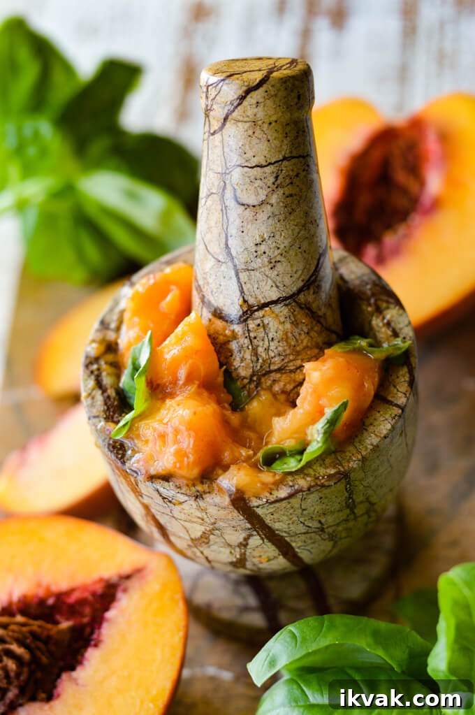 A pestle and mortar muddling fresh peaches and basil. Peach halves and basil is scattered around. 