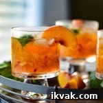 A tray of peach bourbon cocktails with fresh peach slices and fresh basil scattered around.