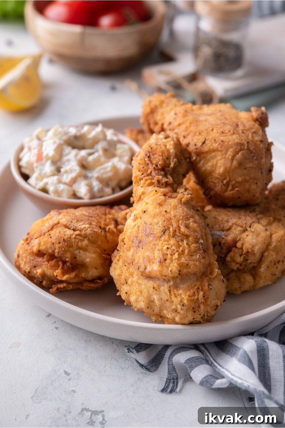 A plate of dark meat fried chicken piled on top of each other with a side of potato salad.