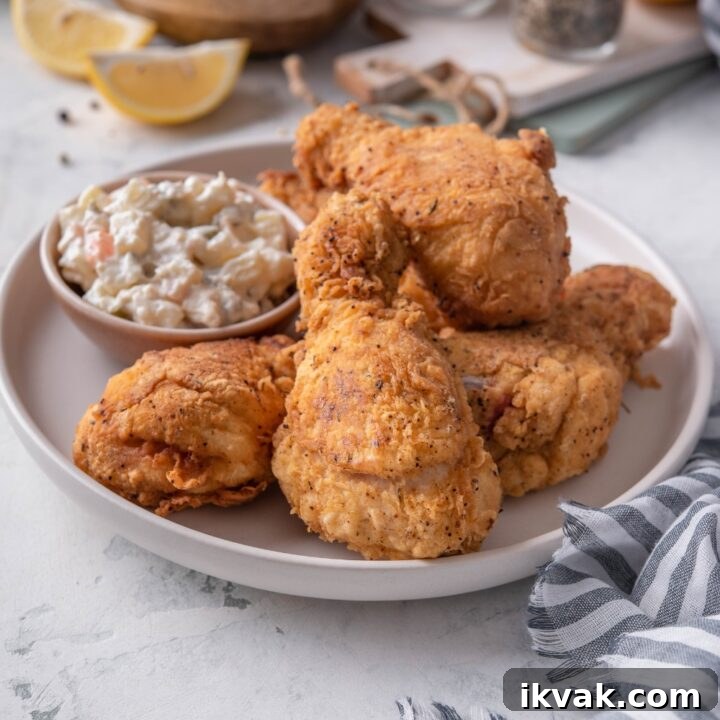 A plate of dark meat fried chicken piled on top of each other with a side of potato salad.