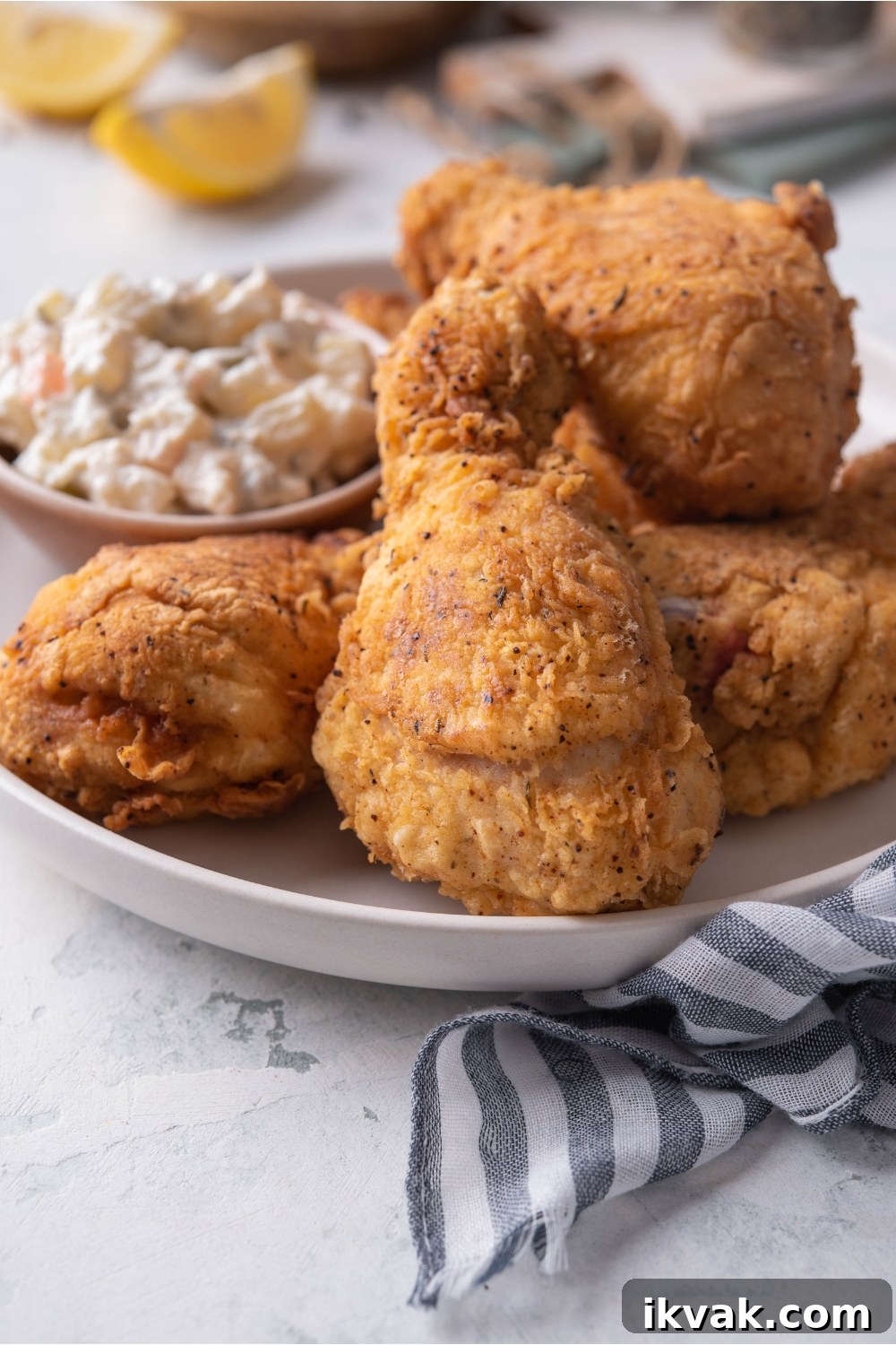 A plate of dark meat fried chicken piled on top of each other with a side of potato salad.