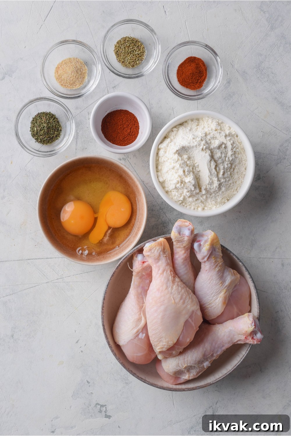 An assortment of ingredients including bowls of raw chicken, two eggs, flour, and spices.