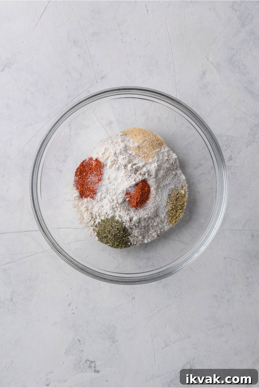 Overhead view of a bowl of flour and spices that have not yet been mixed together.
