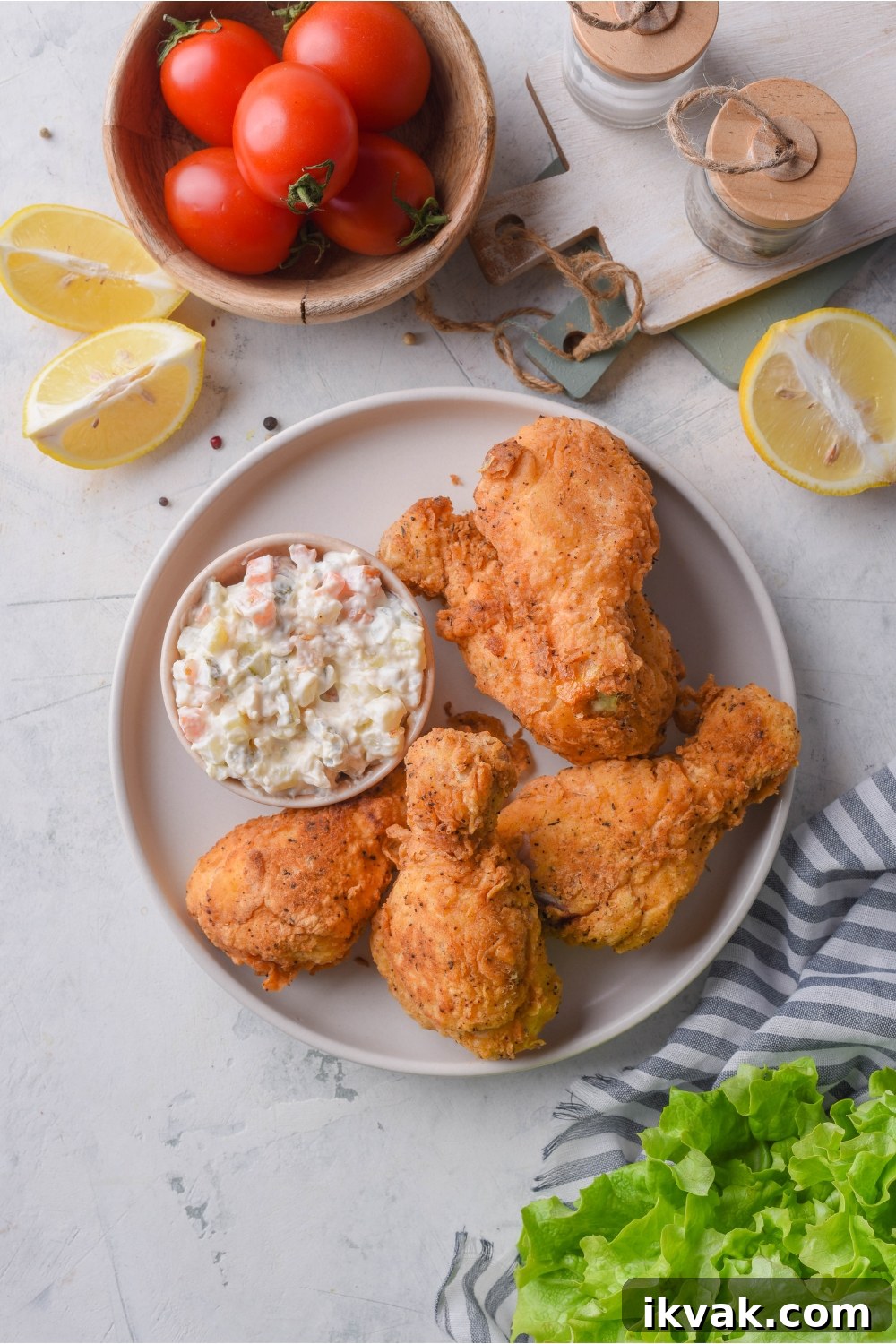Overhead view of four pieces of dark meat fried chicken with a side of creamy salad on the plate.