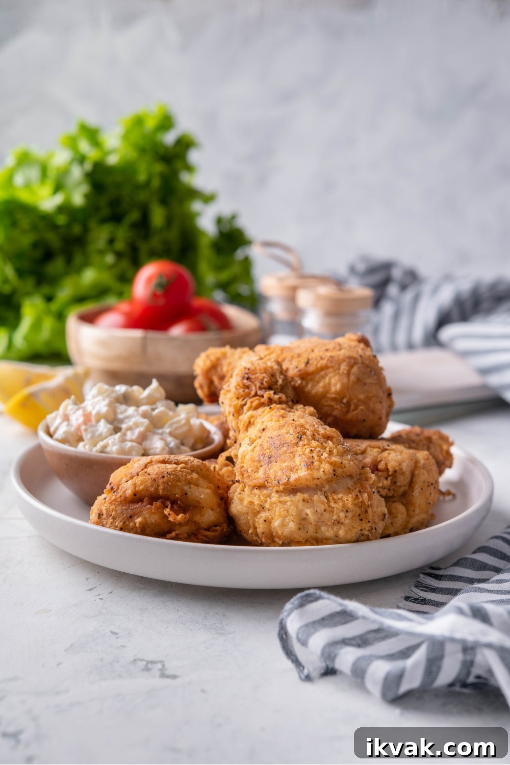 A plate of dark meat fried chicken piled on top of each other with a side of potato salad.