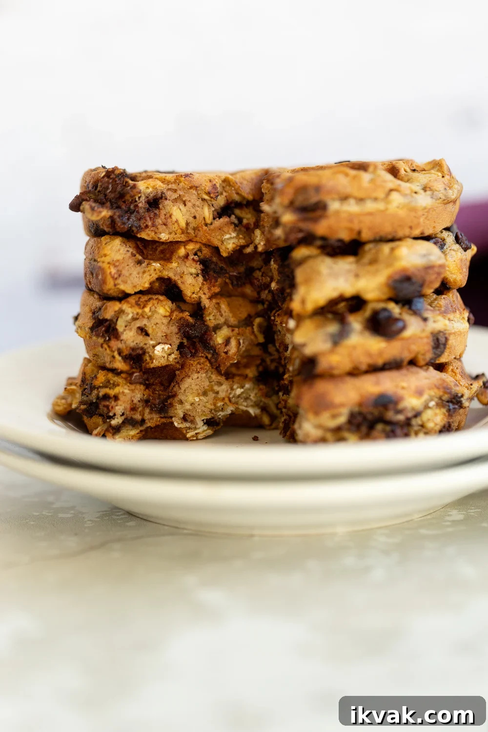 side view of a stack of crispy vegan oatmeal chocolate chip waffles on a white plate