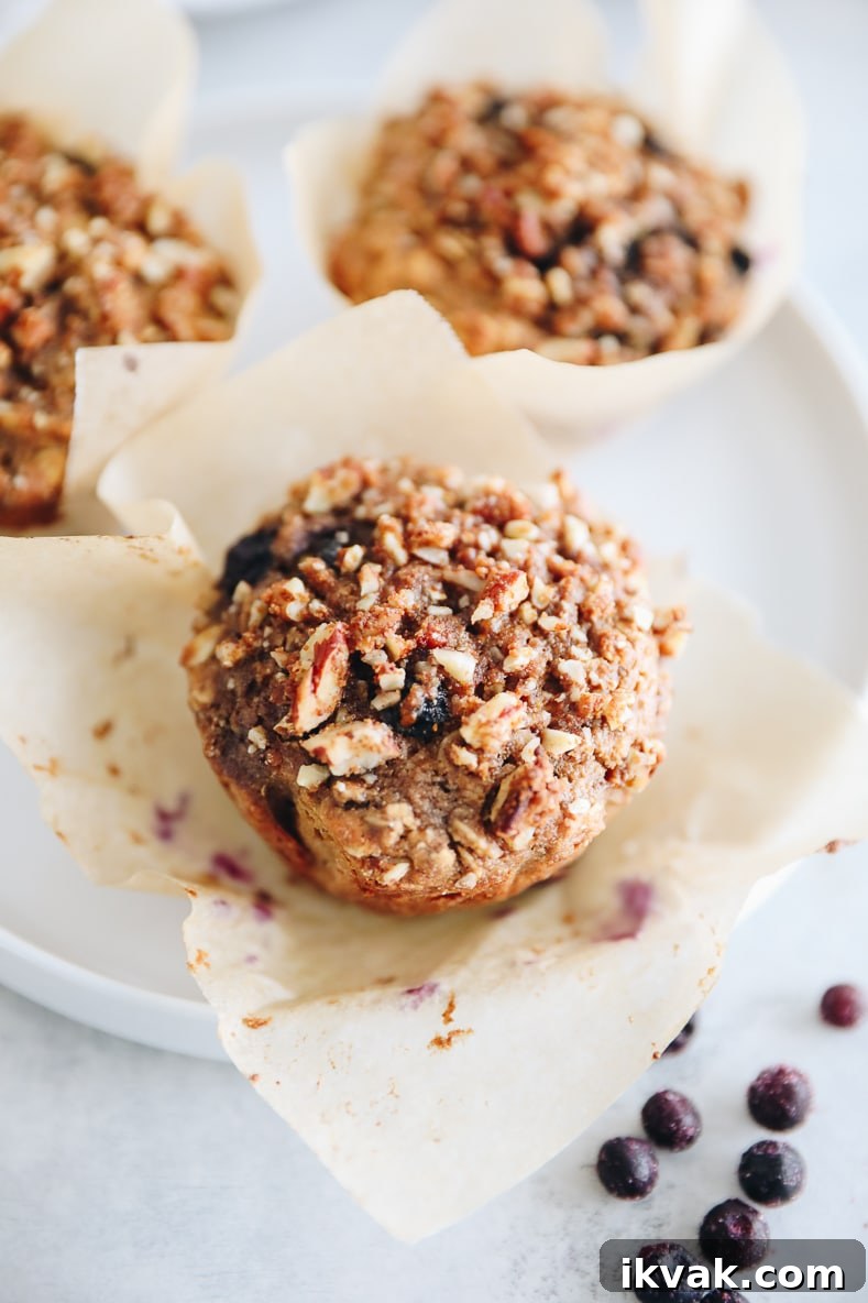 Blueberry Oat Muffins with Oats and Honey Crumble 9 up close of blueberry oat muffins on a white plate with a paper muffin tin.