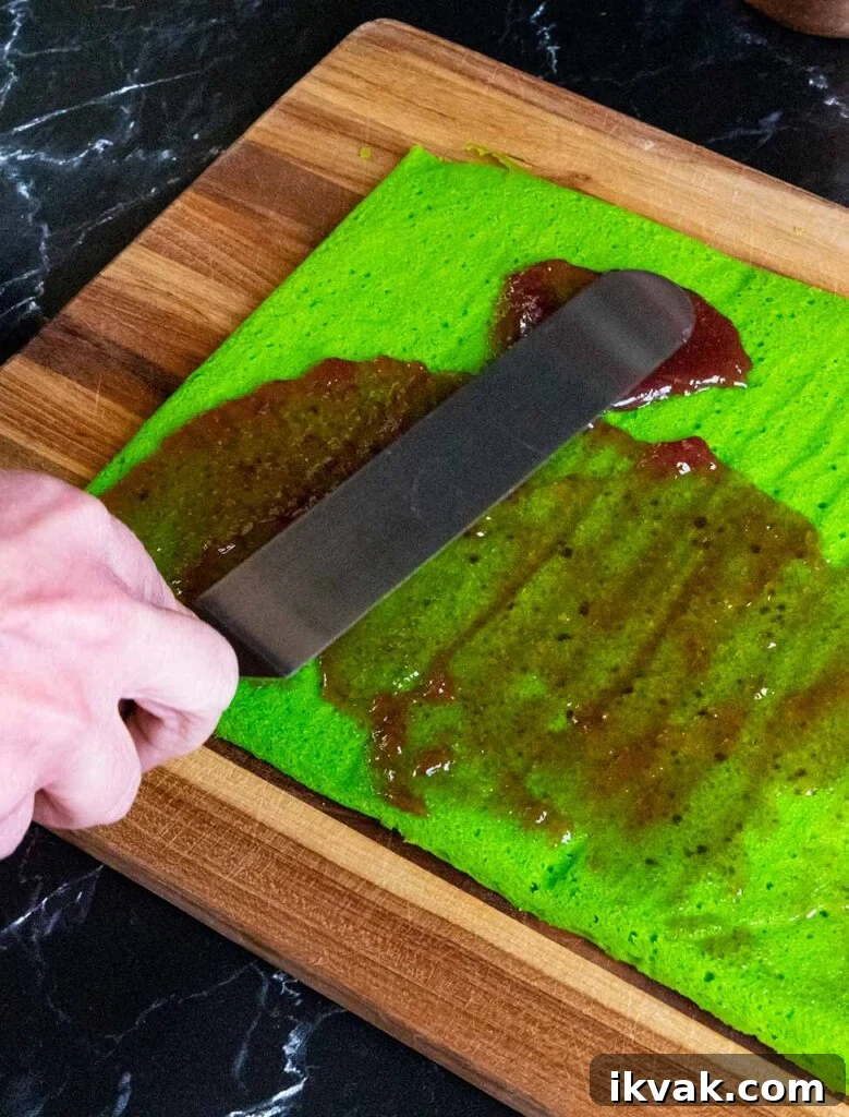 Raspberry jam being spread on the green cookie layer.