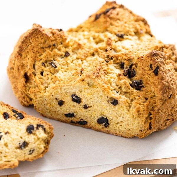 Orange Cherry Irish Soda Bread Recipe for Zesty Homemade Loaf 6 Circular brown colored loaf of bread with one side sliced off all sitting on white pieces of parchment on wood board